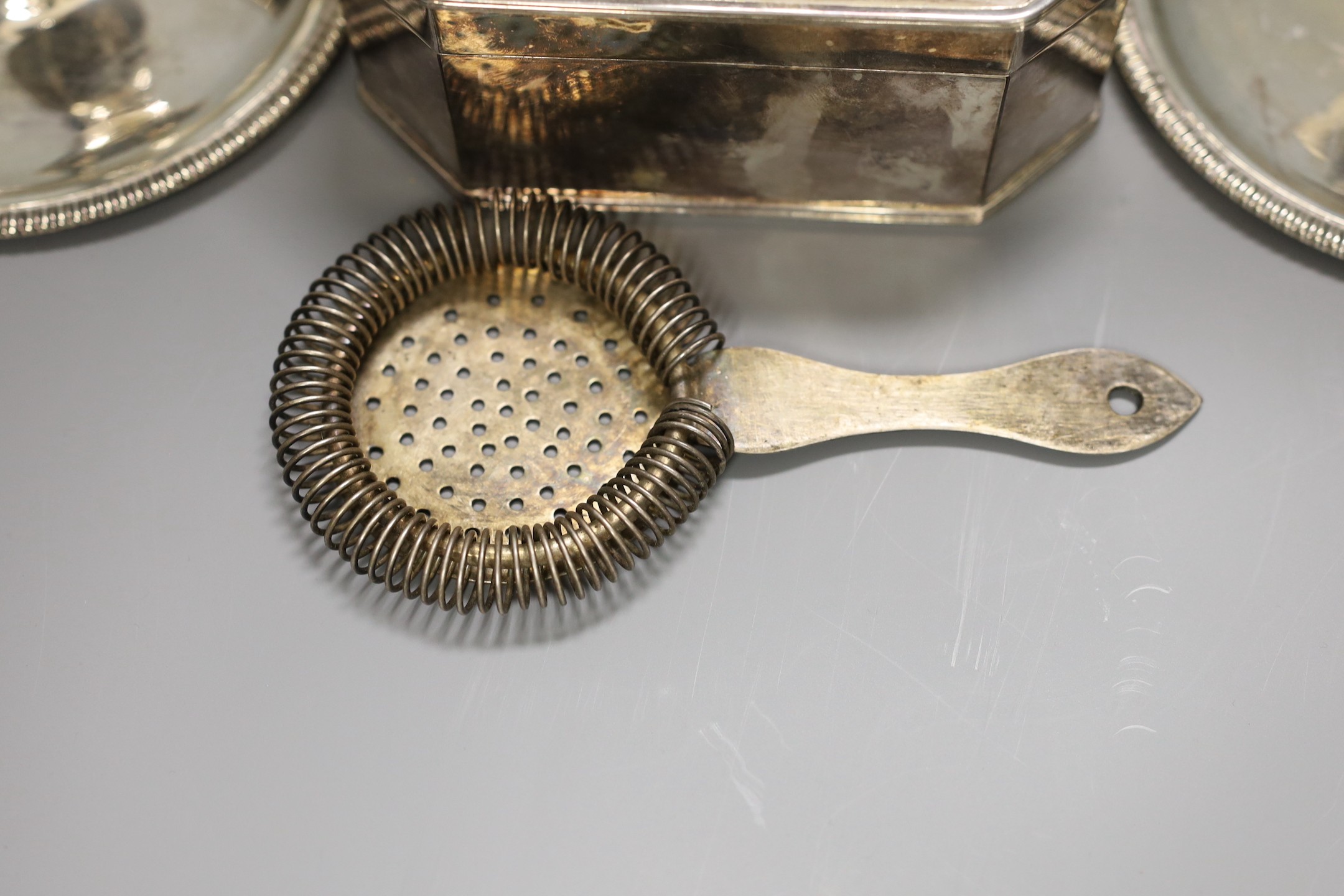 A pair of silver plated chambersticks, a plated octagonal box and cover and a plated strainer.